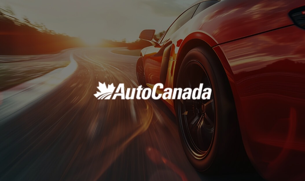 Red sports car driving on highway at sunset with AutoCanada logo overlay, representing a top Canadian automotive group.